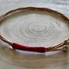 Guitar string bangle wrapped with red wire and tuning pegs still intact